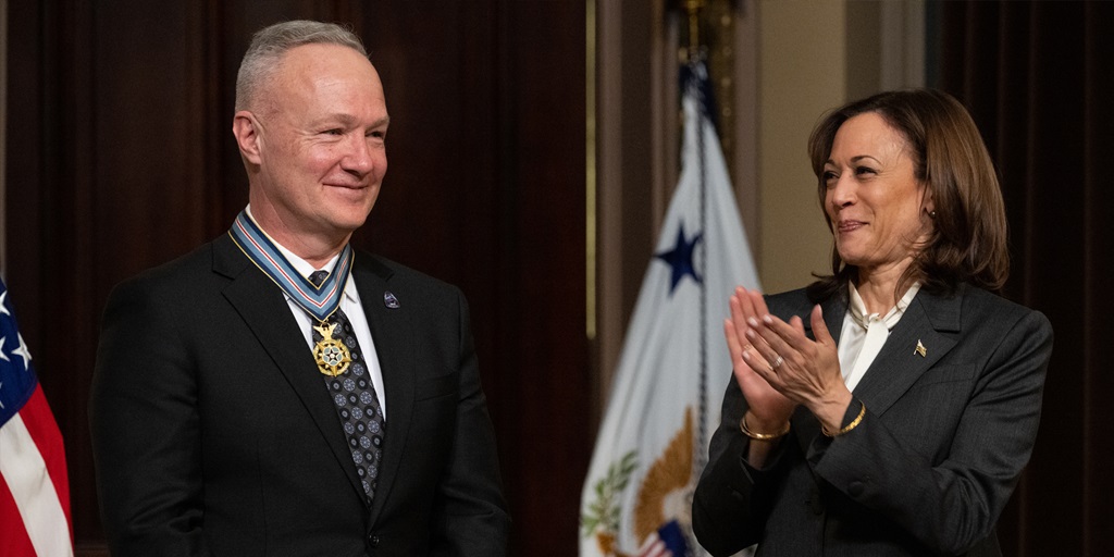 Doug Hurley stands inside the White House after receiving the Congressional Space Medal of Honor; beside him, Vice President Kamala Harris is clapping.