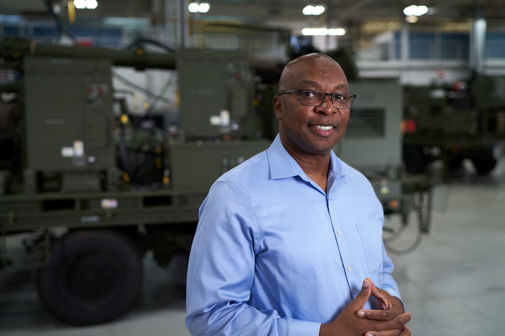 Smiling Employee with glasses wearing blue shirt standing in front of land equipment