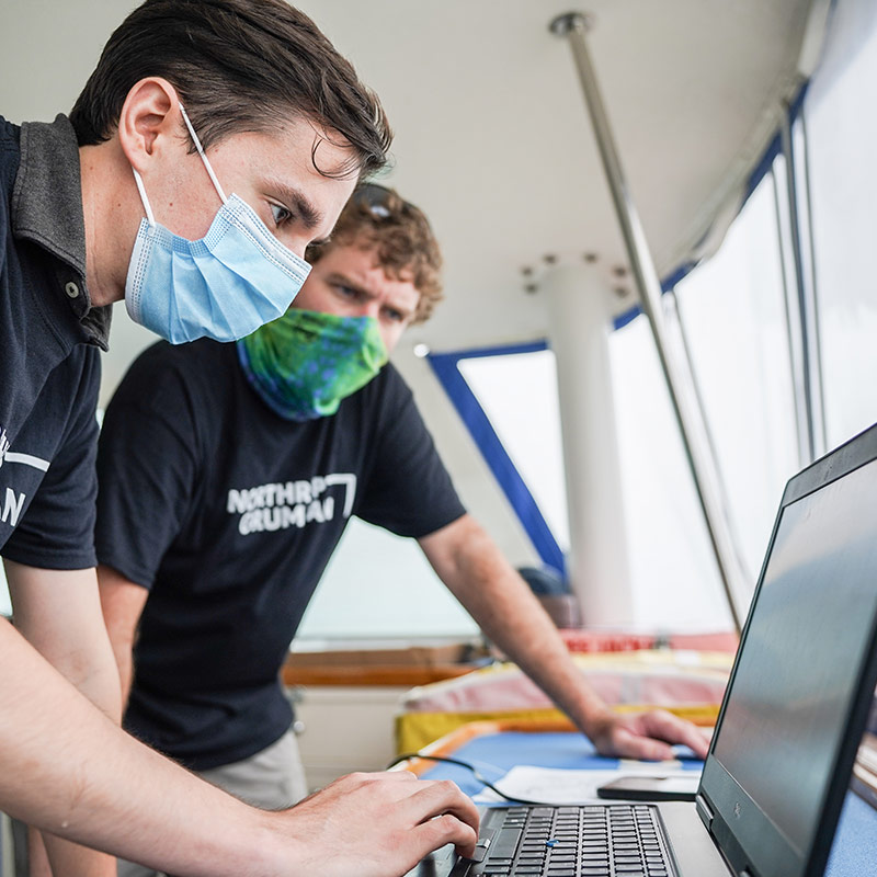 two male Northrop Grumman working on laptop on boat