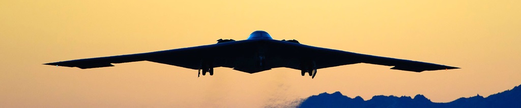 B-2 Spirit airplane flying at dusk with mountain range in background.