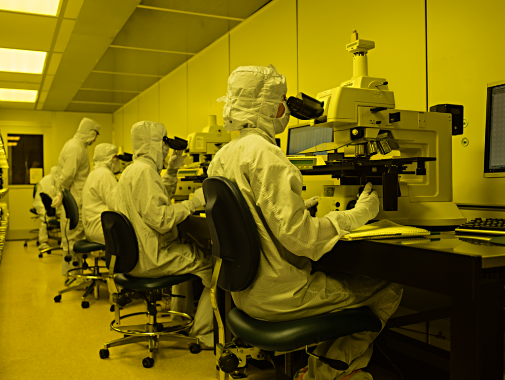 Employees in lab attire use microscopes in a lab