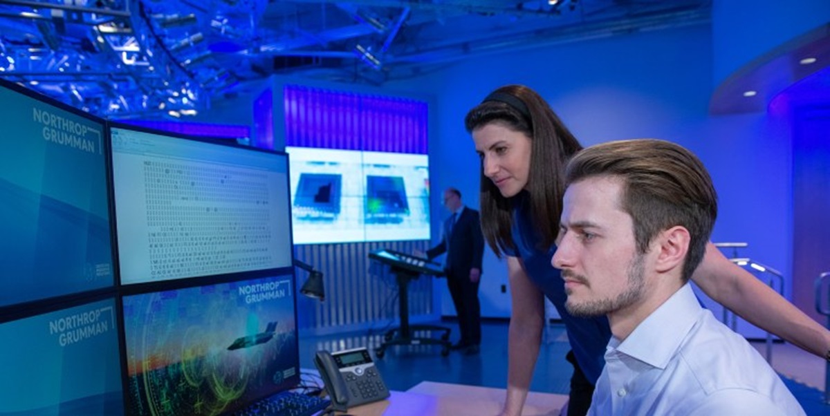 a woman and man look at computer monitors together