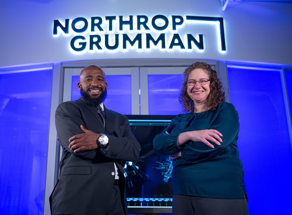 A black man and white woman smile at the camera with a Northrop Grumman logo in the background