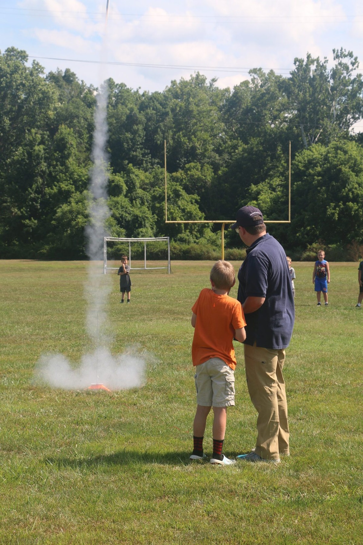 Older man and young child stand outside watching toy rocket fly up