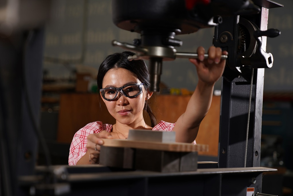 A woman wearing safety goggles works with heavy machinery