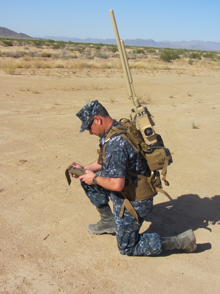 soldier kneeling in desert talking into radio-control device