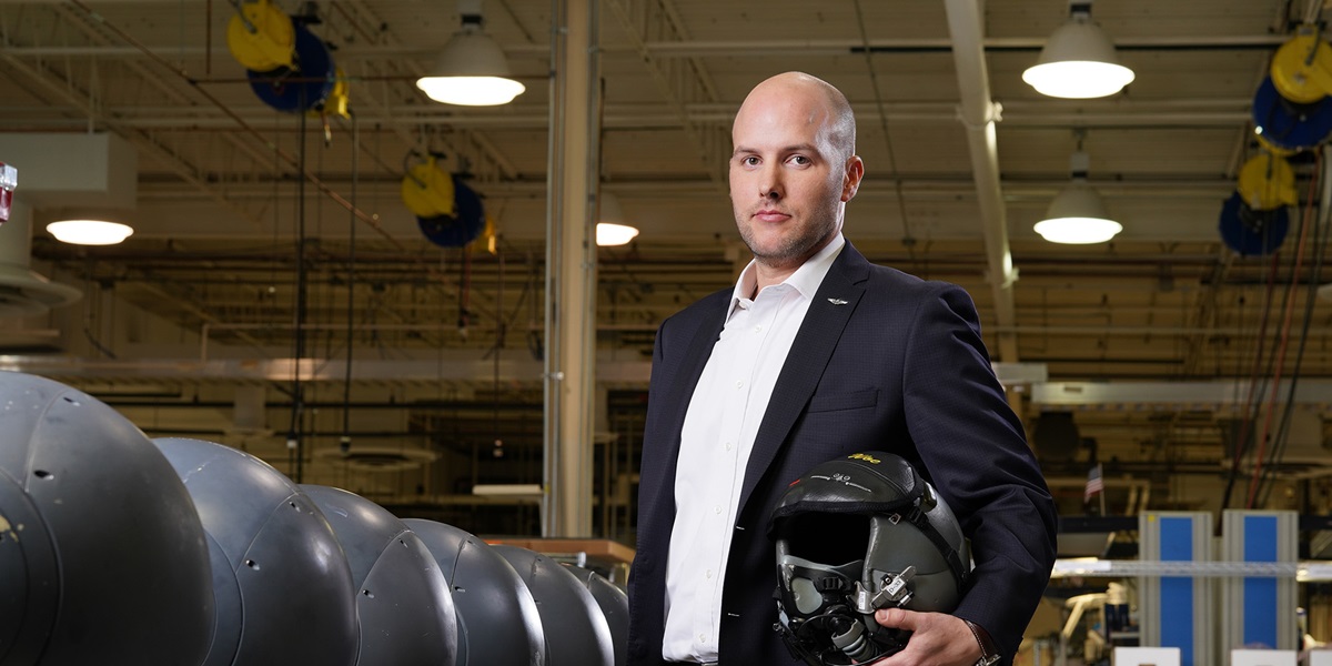 White male holds helmet while standing in manufacturing setting