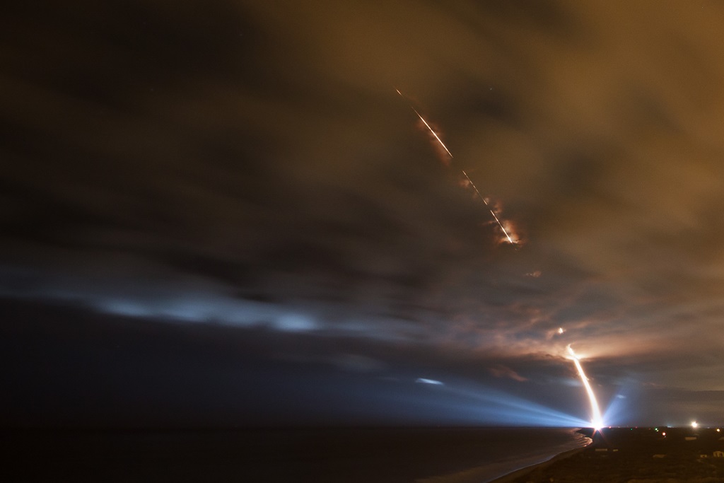 A rocket streak from a rocket launching into Space in front of dark cloudy sky
