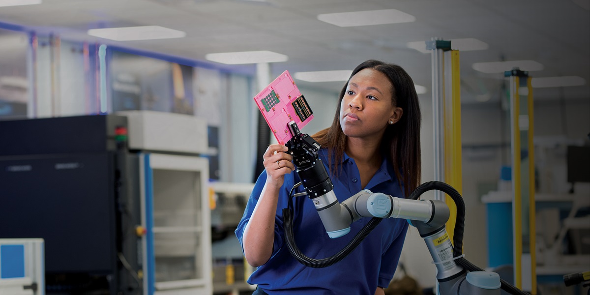 black woman working with robot arm holding microchip