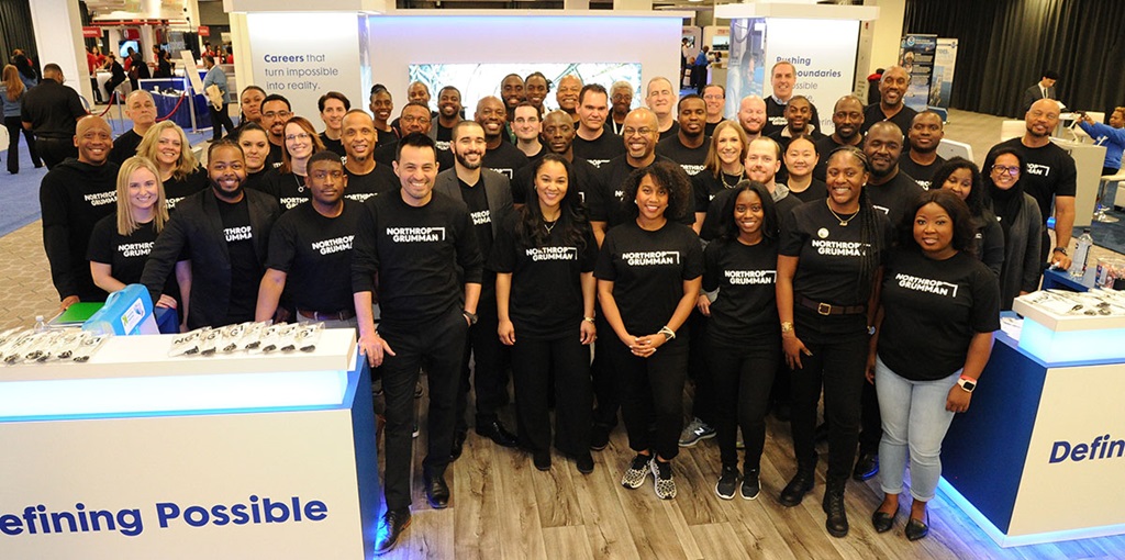 Northrop Grumman employees in black shirts pose at event booth