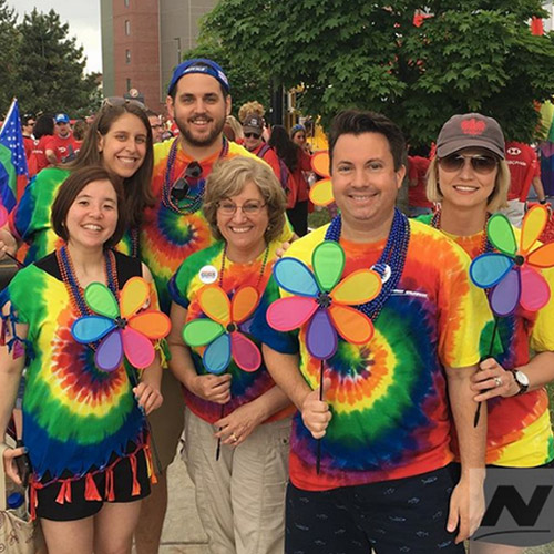 Group of employees wearing rainbow colored tie dye shirts and holding flower windcircles