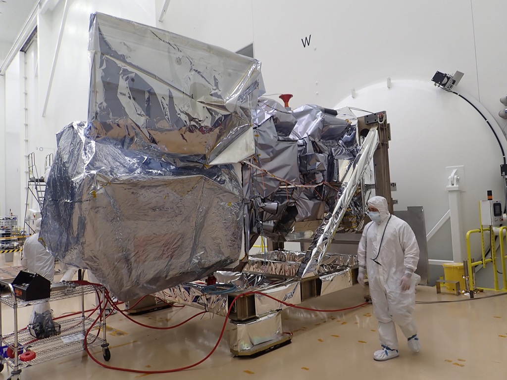 a person in a clean suit walks around a large machine covered in silver foil