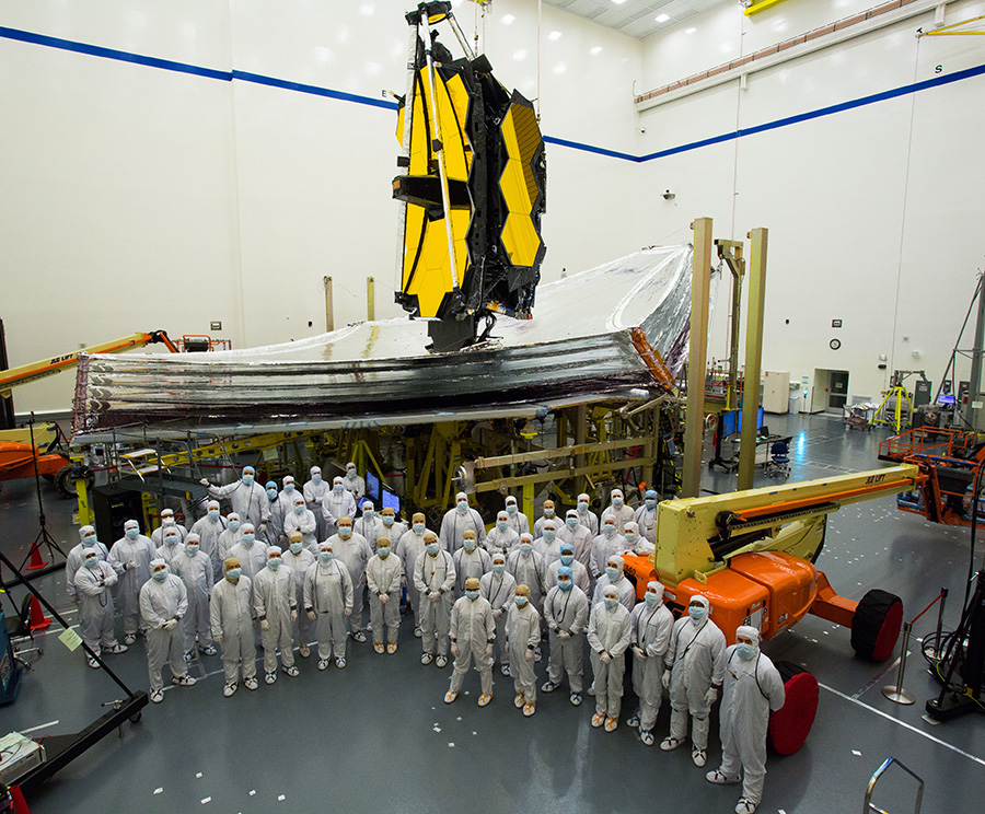 many technicians dressed in bunny suits, pose with the JWST