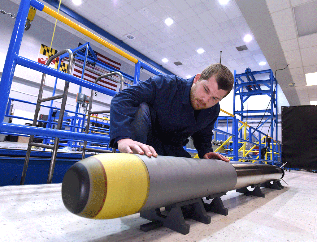 a man stands is bending over to inspect a very light weight torpedo