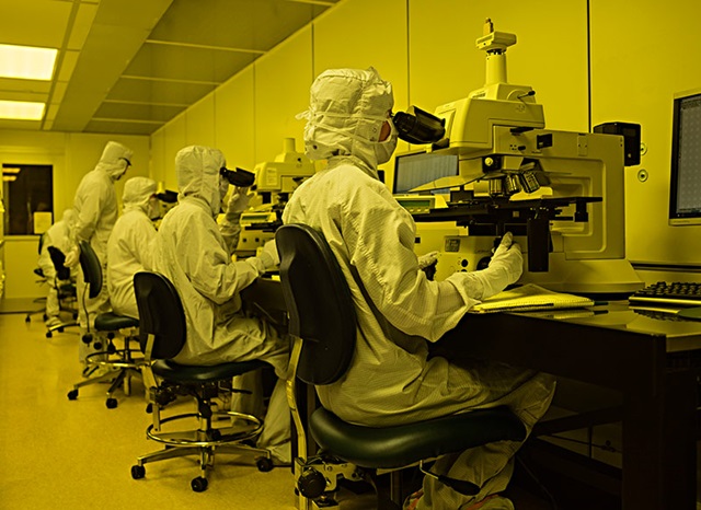 employees in lab attire use microscopes in a lab