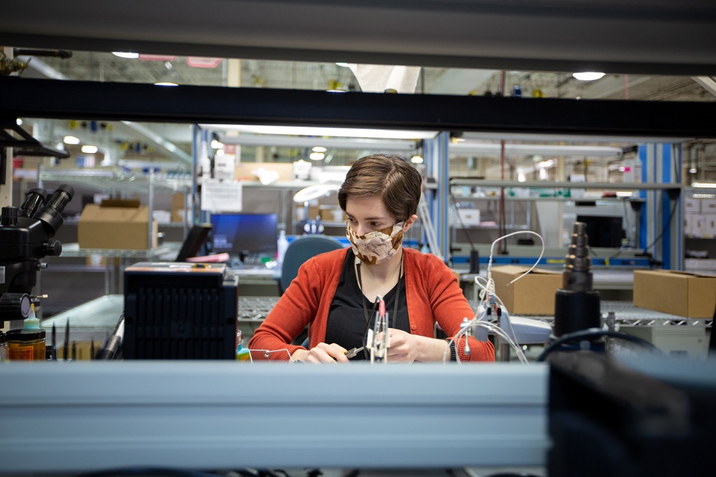 White female wearing mask working in a manufacturing environment.