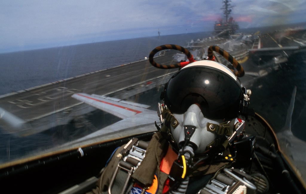 A pilot inside a jet flies away from an aircraft carrier