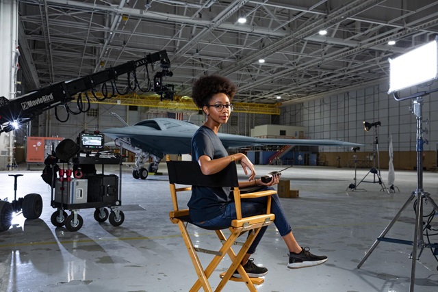 Black woman sitting in chair with aircraft behind her