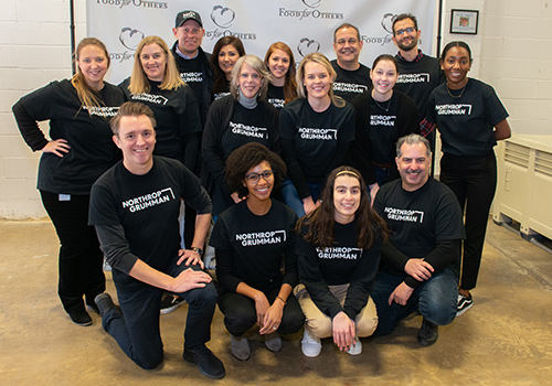 Group photo of employees posing in front of Food for Others banner